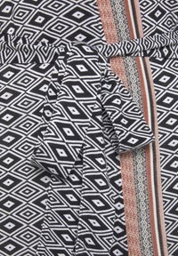 Schwarz-weißer Stoff mit gemusterten Rautensch Formen, ergänzt durch einen kontrastierenden gestreiften Akzent in Rost, Creme und Schwarz an einer Seite.