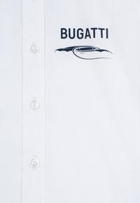 Camicetta bianca con colletto, caratterizzata da un logo nero "BUGATTI" e un design grafico di un'auto. Tessuto liscio e strutturato con bottoni trasparenti.