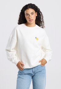 White sweatshirt made of cotton with a round neck and relaxed fit. Features a small embroidered lemon design on the left chest area.