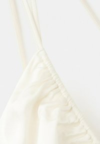 Gros plan sur un tissu blanc présentant un détail froncé et des fines bretelles réglables sur un vêtement.