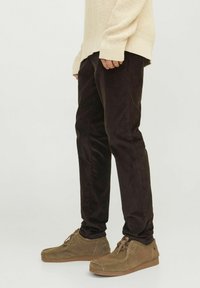Pantalon en velours côtelé marron avec une coupe slim, mettant en avant un ribbing vertical prononcé. Accompagné de chaussures en daim tan et d'un pull en tricot beige.