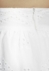 Weißes Baumwollkleid mit bestickten Lochmustern und einem verdeckten Reißverschluss hinten. Weicher Stoff mit einem gerafften Rockdesign.