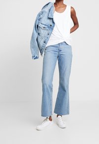Blå denimjacka, vit linne, ljusblå utsvängda jeans och vita sneakers. Jeansen har fransade fållar och en avslappnad passform.