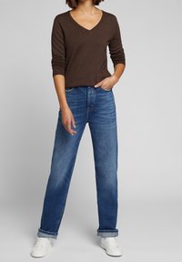 Brązowy długi rękaw V-neck w połączeniu z jasnoniebieskimi spodniami z wysokim stanem, o luźnym kroju i podwiniętych mankietach, dopełnione białymi sneakerami.