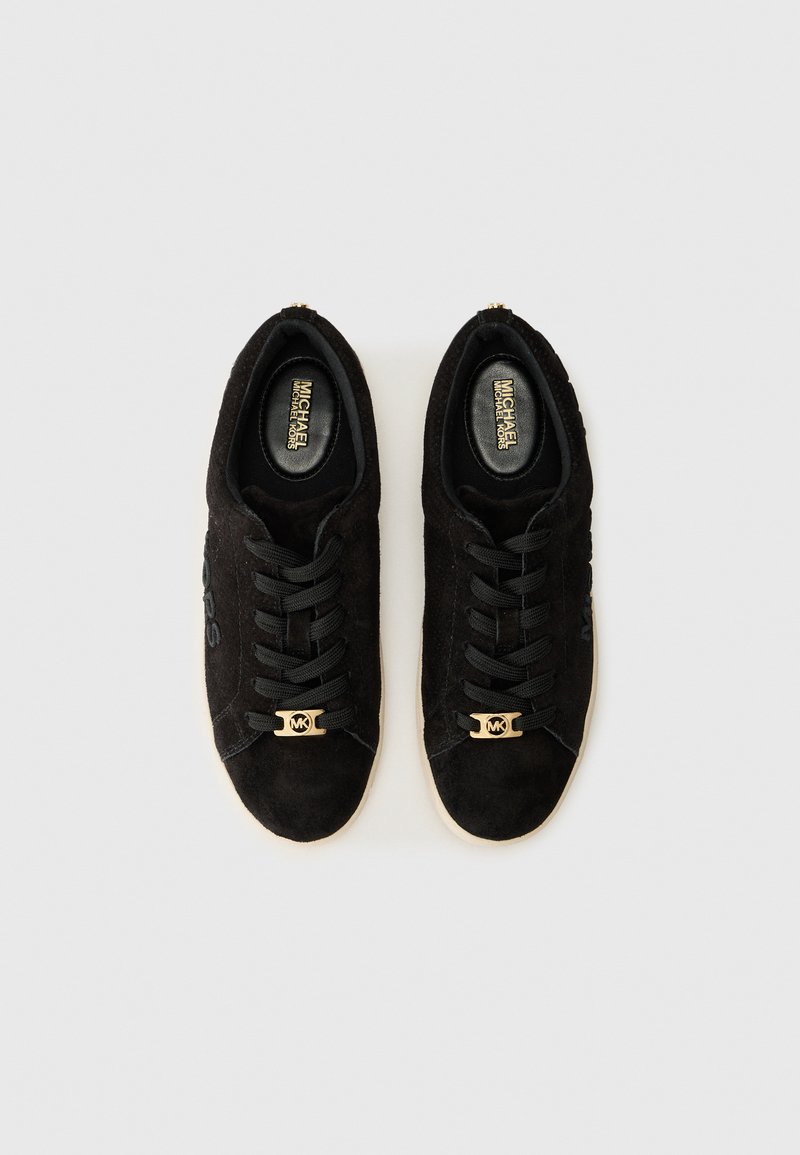 Zwarte suède sneakers met gouden logo en veters, met een klassiek ontwerp en een contrasterende rubberen zool op een lichte achtergrond.