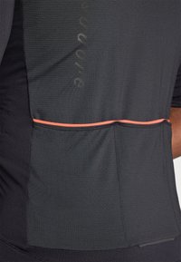 Maglietta atletica grigio scuro con tessuto testurizzato, caratterizzata da una striscia di accento arancione e un sottile dettaglio del logo, progettata per l'abbigliamento sportivo.