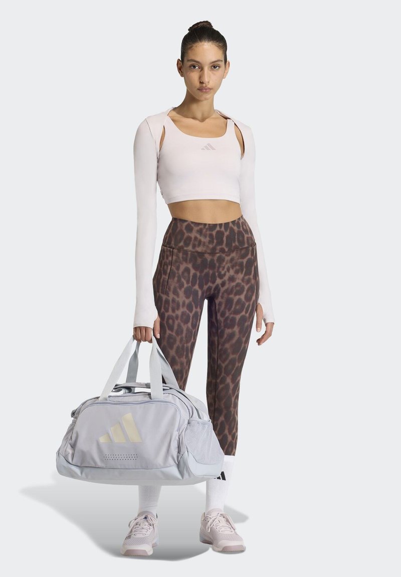 Vaaleanharmaa duffelikassi, jossa on kolme vinoraitaa, leopardi-kuvioidut leggingsit ja vaaleanpunainen lyhyt toppi, jossa on leikkaukset.