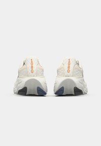 Des chaussures de course de couleur neutre avec un dessus texturé, dotées d'un talon prononcé, d'une semelle en mousse et d'un détail orange "1080" à l'arrière.