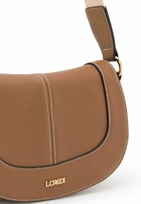 Bruine neplederen schoudertas met witte stiksels, gebogen vorm, verstelbare schouderband en goudkleurig logo-detail aan de voorkant.