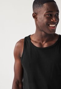 Sort bomuldstanktop med rund halsudskæring og ærmeløs design. Glat tekstur med diskret syningsdetalje.