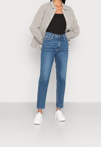 Blå denimjeans med rak benpassform, hög midja och subtila blekningar. I kombination med en grå rutig jacka och vita sneakers.