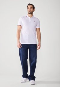 Polo skjorte i hvid bomuld med krave og røde accentstriber. Båret med løstsiddende mørkeblå denim jeans og hvide sneakers.