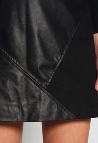 Svart skinnimitation kjol med en texturerad yta, med diagonala sömmar och en asymmetrisk design. Slät yta med lyster.