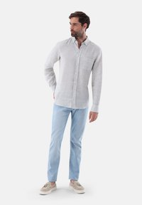 Camicia di lino grigia chiara a maniche lunghe con tasca sul petto, abbinata a jeans azzurri chiari e scarpe slip-on beige.
