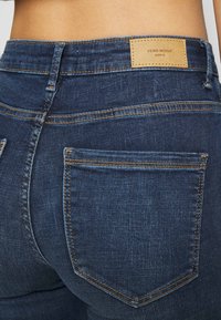 Mörkblå denimjeans med rak passform, synliga sömdetaljer och en tan läderlogotyp på baklinningen.