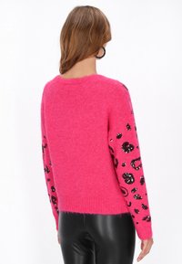 Rosa fluffiger Pullover mit langen Ärmeln und einem schwarzen Pailletten-Leopardenmuster. Gerippter Rundhalsausschnitt und Saum, getragen über enger schwarzen Hosen.