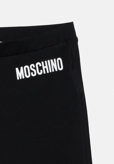 Pantalon en tissu noir avec le logo texte "MOSCHINO" blanc imprimé près du haut sur le côté gauche.
