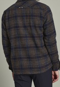 Brun och marinblå rutigt flanellskjorta med en texturerad yta, med krage och knappade ärmslut, visad från baksidan.