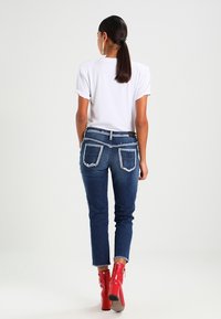 Jeans skinny fit di colore blu scuro con tasche posteriori strappate, abbinati a una maglietta bianca semplice e stivaletti alla caviglia rossi lucidi con tacco alto.