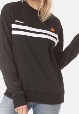 Sudadera negra de ellesse con dos rayas blancas horizontales en el pecho, usada por una persona con vaqueros azul claro.