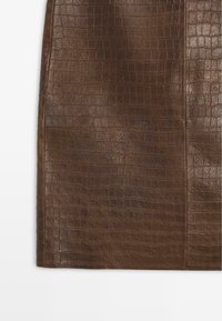 Jupe en cuir marron avec un motif en croco texturé. Design à coupe droite avec des coutures visibles et des bords nets.