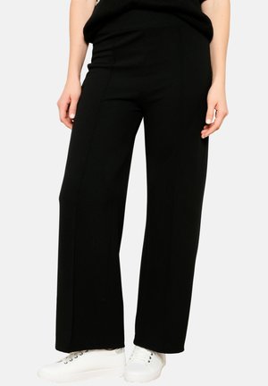 Black wide-leg pants made of soft fabric, featuring a smooth texture and a high waist. Worn with white sneakers for contrast.