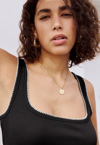 Fekete bordázott trikó négyzet alakú nyakkivágással, fehér cikcakk szegéllyel, arany nyaklánccal és természetes göndör hajjal.