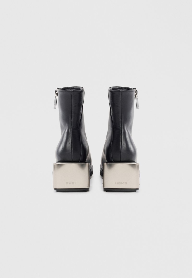 Stivaletti neri in pelle con finitura liscia, dotati di una cerniera bassa sul retro e tacchi a blocco metallici con branding inciso.