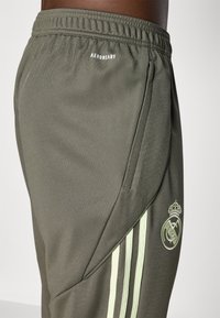 Dark green athletic pants with a textured finish, featuring light green side stripes, a small logo, and an elastic waistband.