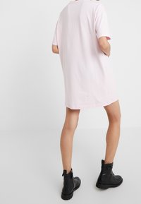 Růžová oversized tričková šaty s krátkými rukávy, hladká bavlněná textura a rovný lem. Nosit s černými koženými kotníkovými botami.
