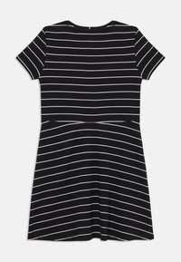 Čierne šaty s krátkym rukávom a vodorovnými bielymi pruhmi, s okrúhlym výstrihom a rozšíreným strihom sukne. Mäkko štruktúrovaná látka.