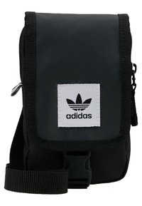 Bolso cruzado de nylon negro con un zipper frontal, correa ajustable y un parche de logo blanco bordado que presenta tres rayas negras.