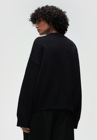 Czarny, oversize sweter o fakturowanym splocie, z okrągłym dekoltem, opadłymi ramionami i ściągaczem na dole. Prosty i nowoczesny design.