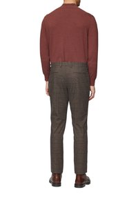 Bordeaux gebreide trui met lange mouwen, gecombineerd met bruine geruite broek. De broek heeft een slim fit en discrete zakken. Bruine leren laarzen maken de outfit compleet.