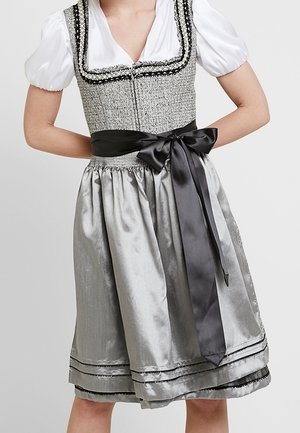 Woman wearing traditional gray dirndl dress with white puffed blouse and black satin bow tied at the waist.