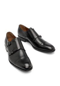 Czarne skórzane buty na nogach z wydłużonym noskiem, z podwójnymi paskami zapinanymi na klamry oraz subtelnym przeszyciem na czubku.