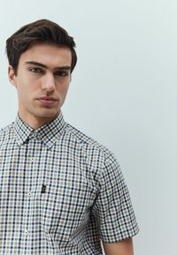 Camicia a maniche corte con bottoni in fantasia a quadri marroni e bianchi, caratterizzata da un colletto strutturato e un piccolo logo sulla tasca.