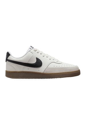 Zapatilla blanca de cuero con swoosh negro, suela de goma crema, punta redonda, parte superior perforada y cordones planos. Sutiles acentos de costura en los lados.