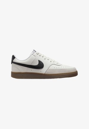 Zapatilla blanca de cuero con swoosh negro, suela de goma crema, punta redonda, parte superior perforada y cordones planos. Sutiles acentos de costura en los lados.