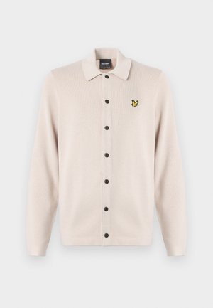 Jasno-beżowy kardigan z kołnierzykiem, z rzędem czarnych guzików i małym żółtym logo ptaka na lewej piersi.