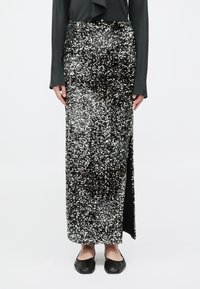 Gonna maxi nera in paillettes con uno spacco laterale, caratterizzata da una texture lucida e una silhouette aderente. Abbinata a ballerine nere.