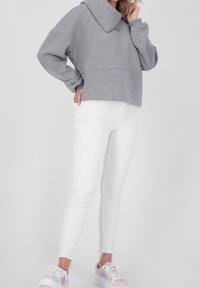 Grauer, übergroßer Pullover mit weitem Kragen, kombiniert mit weißen Skinny-Jeans. Die Sneakers haben ein holografisches Design.