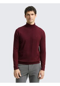 Bordeauxroter Rollkragenpullover aus weichem Stoff, mit langen Ärmeln und einem gerippten Kragen, kombiniert mit grauer Hose.