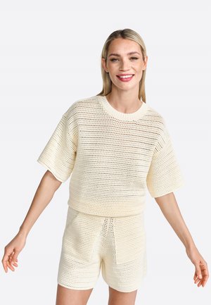 Ensemble tricoté en deux pièces en crème clair, composé d'un haut ample à manches courtes et de shorts assortis avec poches, mettant en valeur un tissage ouvert texturé.