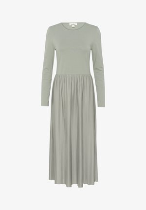 Šviesiai žalia suknelė su ilgomis rankovėmis, turinti prigludusią viršutinę dalį ir klostuotą sijoną. Pagaminta iš minkštos medžiagos su lygiu paviršiumi ir kasdiene dizaino estetiką.