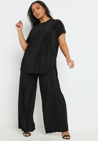 Svart plisserad topp och vidbyxor-set, med texturerad tyg, korta ärmar och sidofickor. Matchat med svarta klacksandaler.