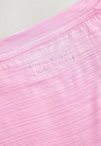 Gros plan d’un tissu rose avec bord cousu et lettres en relief épelant "ACTIVE" dans un contour rectangulaire.
