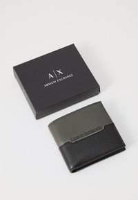 Black and olive green leather wallet with textured surfaces and embossed "Armani Exchange" logo, presented in a black box.