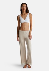 Bílá bezrukávová braletka s V-výstřihem a béžové, volné kalhoty se krajkovým lemem na spodním okraji. Měkká látka, uvolněný střih, lehká textura.