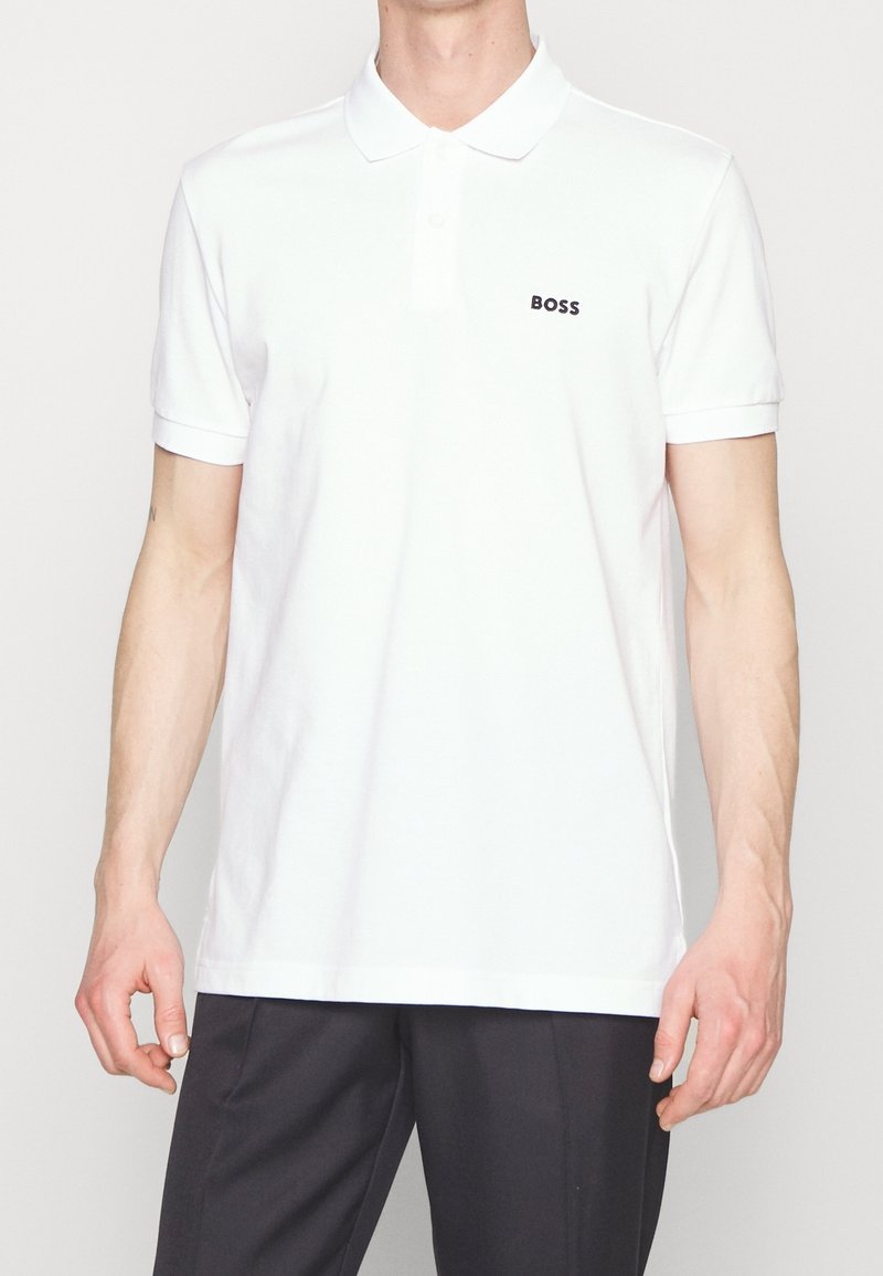 Vit polo med klassisk krage och korta ärmar. Har en liten svart "BOSS"-logotyp på vänster bröst. Tillverkad av mjukt, glatt tyg.